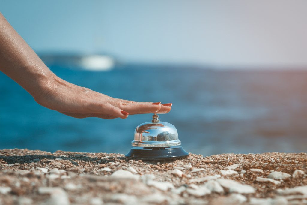 A hand ringing a silver service bell on the shore
